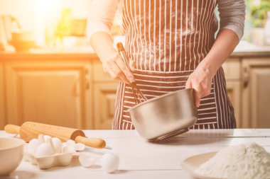 Kase hamur ve çırpma teli, closeup ile tutan genç kadın. Çizgili bir önlük bir kadın mutfakta yemek