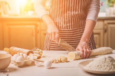 İki kadının el görünümünü yakın çekim bıçak hamur kesme. Çizgili bir önlük bir kadın mutfakta yemek