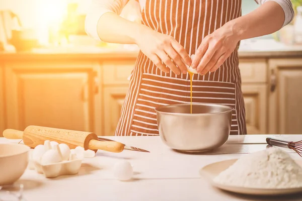Genç kadın üzerinde hamur, bir kase yumurta kırma yakın çekim. Çizgili bir önlük bir kadın mutfakta yemek