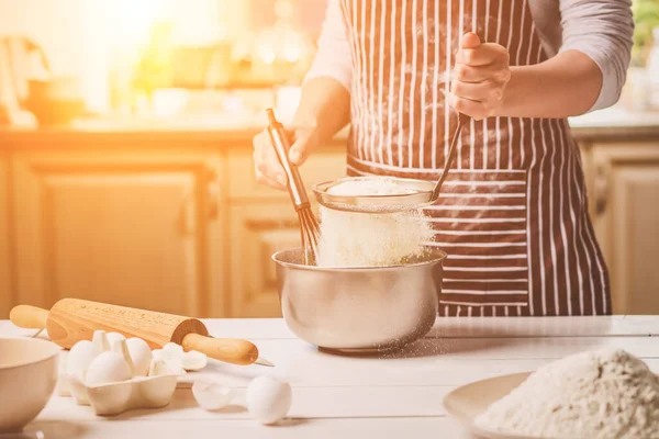 Kase hamur ve çırpma teli, closeup ile tutan genç kadın. Çizgili bir önlük bir kadın mutfakta yemek