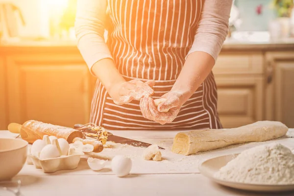 Kadın fırında pasta. Pudra tatlılar yapar. Çörekler yapma. Hamur masanın üzerinde. Hamur yoğurmak. Çizgili bir önlük bir kadın mutfakta yemek