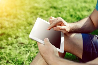 Casual giyimli genç adam parkta otururken modern dijital tablet kullanarak close-up, yenilikçi bağlantı sosyal ağ dışında güneş ışığı dostum. Güneş parlaması