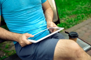 Man sitting on a bench and using a digital tablet. Mens hands closeup