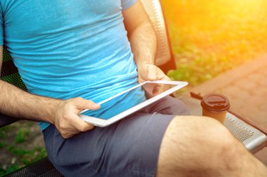 Man sitting on a bench and using a digital tablet. Mens hands closeup. Sun flare