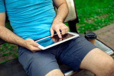 Man sitting on a bench and using a digital tablet. Mens hands closeup