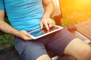Man sitting on a bench and using a digital tablet. Mens hands closeup. Sun flare
