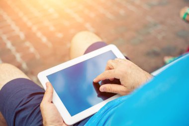 Man sitting on a bench and using a digital tablet. Mens hands closeup. Sun flare