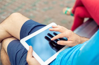 Man sitting on a bench and using a digital tablet. Mens hands closeup