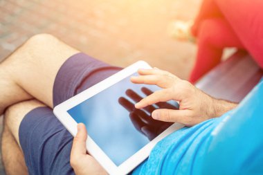Man sitting on a bench and using a digital tablet. Mens hands closeup. Sun flare