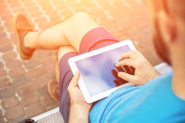 Man sitting on a bench and using a digital tablet. Mens hands closeup. Sun flare