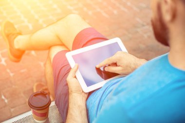 Man sitting on a bench and using a digital tablet. Mens hands closeup. Sun flare