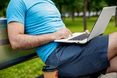 Close-up shot of handsome mans hands touching laptop computers screen. Businessman using a laptop computer and sitting on a bench.
