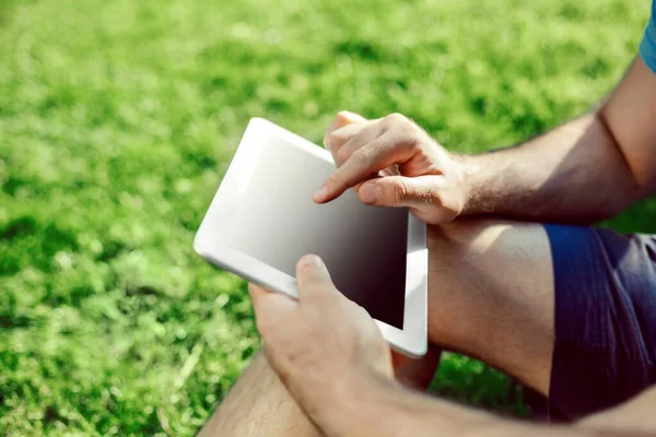 Casual giyimli genç adam parkta otururken modern dijital tablet kullanarak close-up, hipster adam bağlayan sosyal ağ dışında güneş ışığı