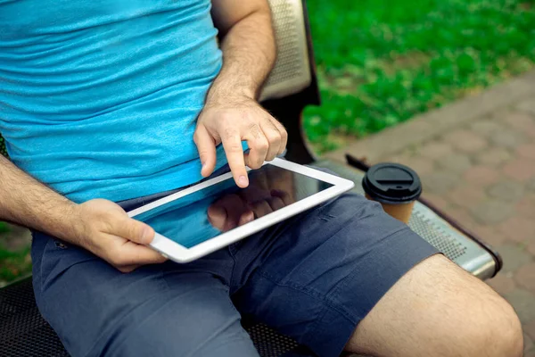 Man sitting on a bench and using a digital tablet. Mens hands closeup