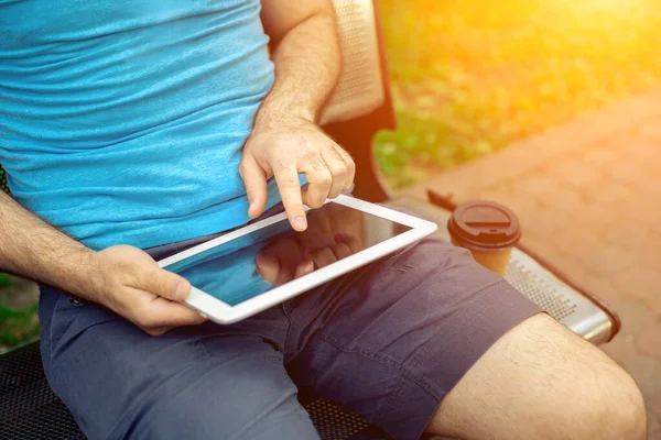 Man sitting on a bench and using a digital tablet. Mens hands closeup. Sun flare