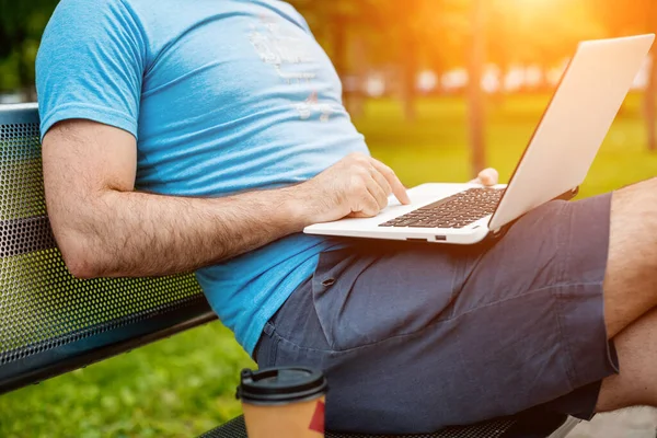 Close-up shot of handsome mans hands touching laptop computers screen. Businessman using a laptop computer and sitting on a bench.. Sun flare