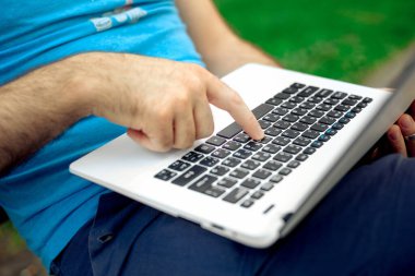 Close-up shot of handsome mans hands touching laptop computers screen. Businessman using a laptop computer and sitting on a bench.