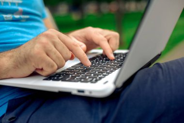 Close-up shot of handsome mans hands touching laptop computers screen. Businessman using a laptop computer and sitting on a bench.