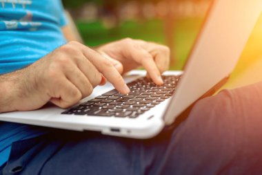Close-up shot of handsome mans hands touching laptop computers screen. Businessman using a laptop computer and sitting on a bench.. Sun flare