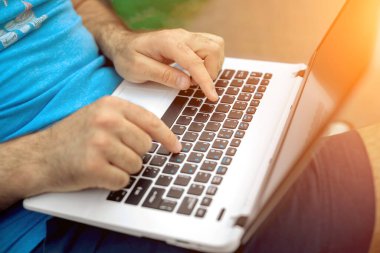 Close-up shot of handsome mans hands touching laptop computers screen. Businessman using a laptop computer and sitting on a bench.. Sun flare