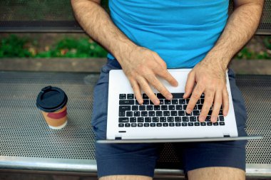 Close-up shot of handsome mans hands touching laptop computers screen. Businessman using a laptop computer and sitting on a bench.