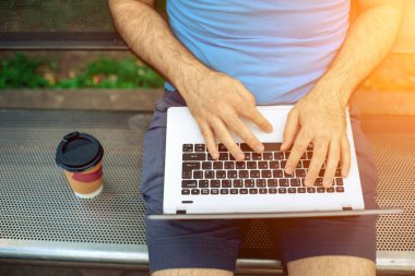 Close-up shot of handsome mans hands touching laptop computers screen. Businessman using a laptop computer and sitting on a bench.. Sun flare