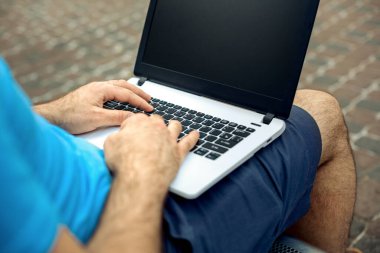 Close-up shot of handsome mans hands touching laptop computers screen. Businessman using a laptop computer and sitting on a bench.