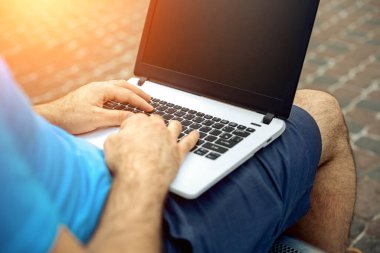 Close-up shot of handsome mans hands touching laptop computers screen. Businessman using a laptop computer and sitting on a bench.. Sun flare