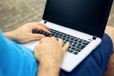 Close-up shot of handsome mans hands touching laptop computers screen. Businessman using a laptop computer and sitting on a bench.