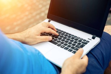 Close-up shot of handsome mans hands touching laptop computers screen. Businessman using a laptop computer and sitting on a bench.. Sun flare