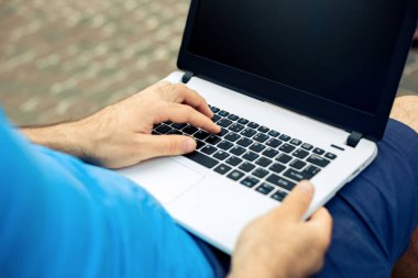 Close-up shot of handsome mans hands touching laptop computers screen. Businessman using a laptop computer and sitting on a bench.