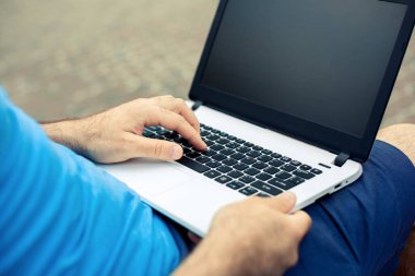 Close-up shot of handsome mans hands touching laptop computers screen. Businessman using a laptop computer and sitting on a bench.