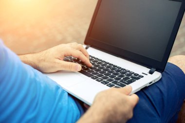 Close-up shot of handsome mans hands touching laptop computers screen. Businessman using a laptop computer and sitting on a bench.. Sun flare