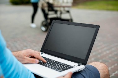 Close-up shot of handsome mans hands touching laptop computers screen. Businessman using a laptop computer and sitting on a bench.