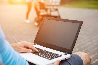 Close-up shot of handsome mans hands touching laptop computers screen. Businessman using a laptop computer and sitting on a bench.. Sun flare