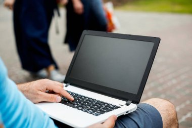 Close-up shot of handsome mans hands touching laptop computers screen. Businessman using a laptop computer and sitting on a bench.