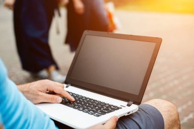 Close-up shot of handsome mans hands touching laptop computers screen. Businessman using a laptop computer and sitting on a bench.. Sun flare