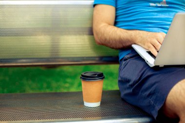 Freelance work. Casual dressed man sitting at wooden beanch inside garden working on computer.