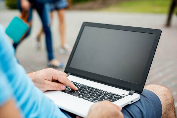 Close-up shot of handsome mans hands touching laptop computers screen. Businessman using a laptop computer and sitting on a bench.