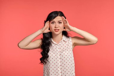 Stüdyoda, beyaz benekli bluz giyen zarif ergen bir kızın fotoğrafı. Küçük esmer kadın üzgün görünüyor ve pembe bir arka planda poz veriyor. İnsanlar ve samimi duygular.