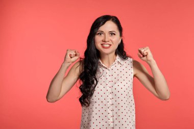 Stüdyo resmi, sıradan beyaz benekli bluz giyen güzel bir kadın. Küçük esmer kadın mutlu görünüyor, pembe arka planda poz veriyor. İnsanlar ve samimi duygular.