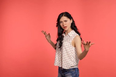 Güzel bir genç kızın atölye fotoğrafı üzgün görünüyor, günlük beyaz benekli bluz ve kot şort giyiyor. Küçük esmer kadın mutsuz, pembe arka planda poz veriyor. İnsanlar ve