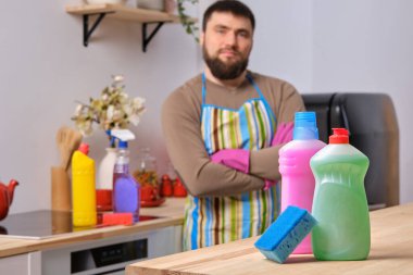 Beyaz sakallı adam arka planda kollarını kavuşturmuş duruyor ve ön planda bez olan farklı deterjanların reklamını yapıyor.