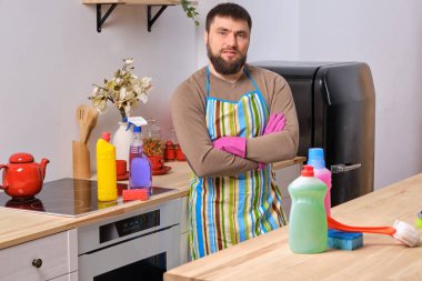 Beyaz sakallı adam arka planda kollarını kavuşturmuş duruyor ve ön planda bez olan farklı deterjanların reklamını yapıyor.