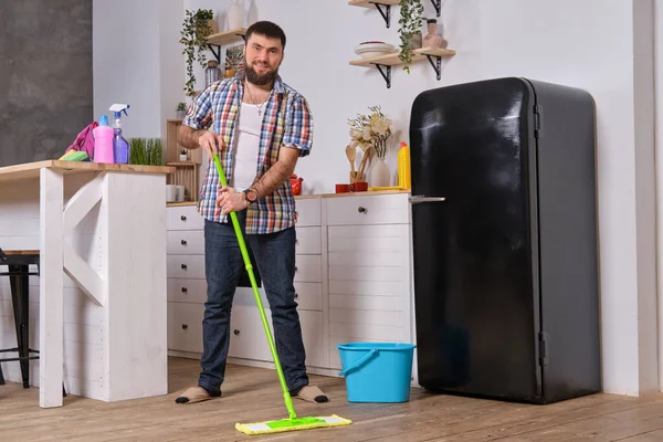 客房和清洁概念 英俊的胡子丈夫打扫厨房 年轻的快乐男子与绿色拖把很高兴帮助做家务 — 图库照片