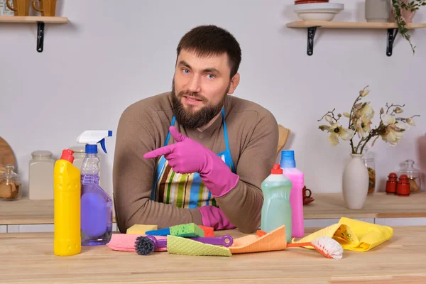 Image of a young Caucasian bearded man in the kitchen, he makes little presentation of all his detergents, preparing for big cleaning
