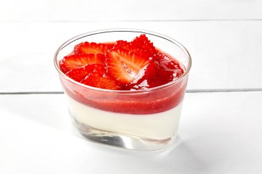 Üzerine çilek ve ravent püresi katmanı ve beyaz ahşap masadaki cam tatlı kasesinde servis edilen taze böğürtlen dilimleri serpiştirilmiş kremalı panna cotta. Popüler İtalyan tatlıları