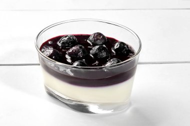 Hafif aromalı kremalı panna cotta üzerine yaban mersini ve lavanta soslu beyaz ahşap zemin üzerinde cam servis edilir. İtalyan tatlısı. Doğal organik tatlılar.