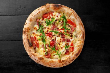 Lezzetli taze İtalyan Boscaiola pizzası krema sosu, mozzarella, kababanossi ve salam dilimleri, mantarlar, parmesan renginde siyah ahşap yüzeyde taze roka yaprakları.