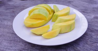Olgun mango dilimleri eski ahşap bir zemine yerleştirilmiş beyaz bir tabakta, yiyecek ve meyve iyi sağlık için vitaminlerle doludur..